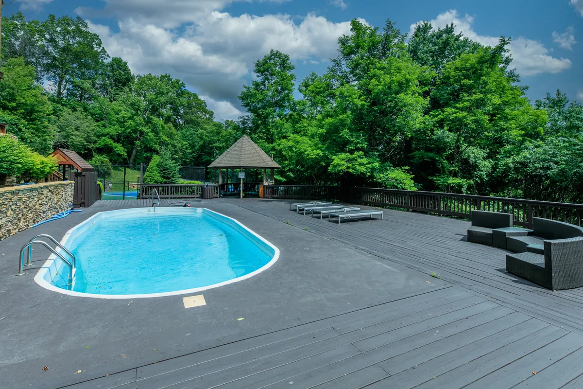 This image highlights a sparkling swimming pool surrounded by outdoor seating, a wooden deck, and mature trees, creating a relaxing oasis perfect for both sunbathing and social gatherings. The inviting scene suggests a place for guests of all ages to unwind by the water or enjoy meals al fresco.