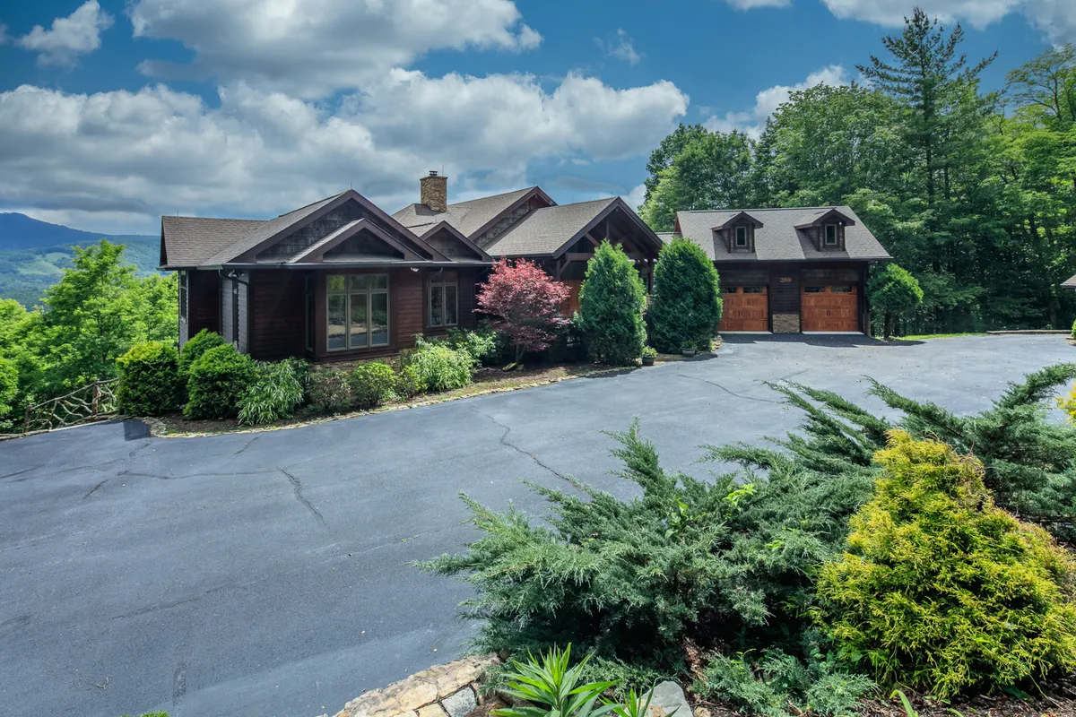 A wide exterior view of the main house and garage, surrounded by lush greenery and set against a backdrop of rolling hills. The expansive lawn and landscaping evoke a tranquil, inviting atmosphere, hinting at the home's connection to nature and the greater High Country beyond.