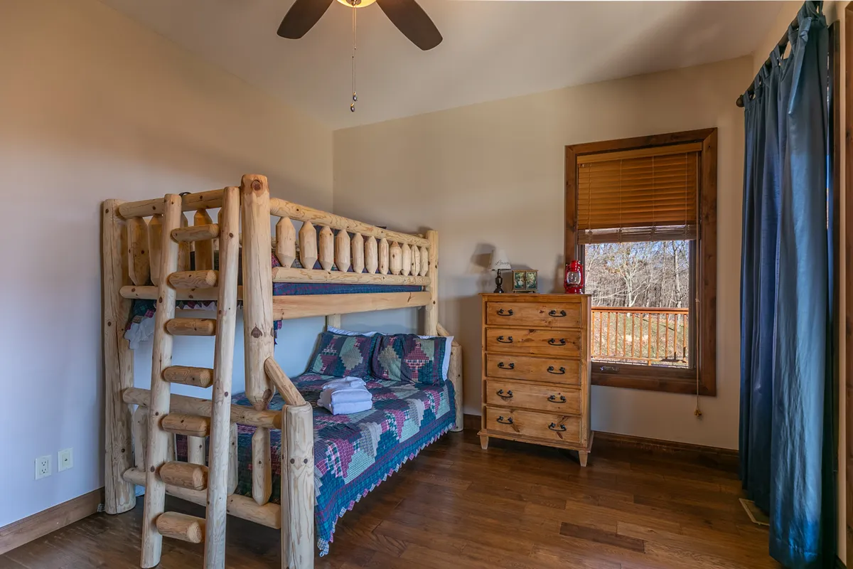 A warm and inviting bunk room featuring a sturdy bunk bed, a wooden dresser, and a window with views. The bedding and playful accents make this space perfect for younger guests, adding a fun, family-friendly atmosphere.