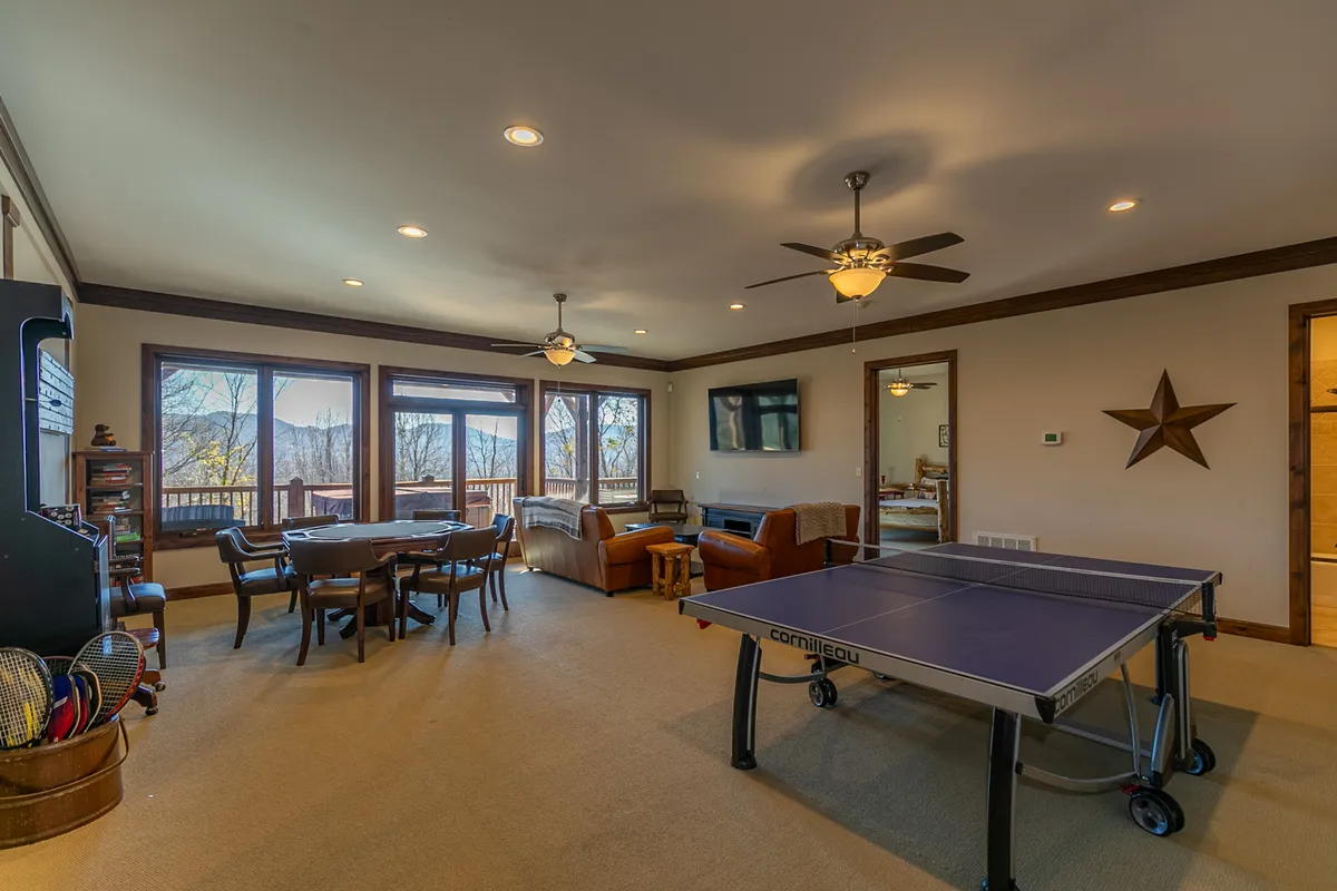 A spacious secondary living area with a ping pong table, comfortable seating, large windows framing mountain views, and a dining table nearby. The scene is lively and welcoming, ideal for family game nights and relaxed gatherings.