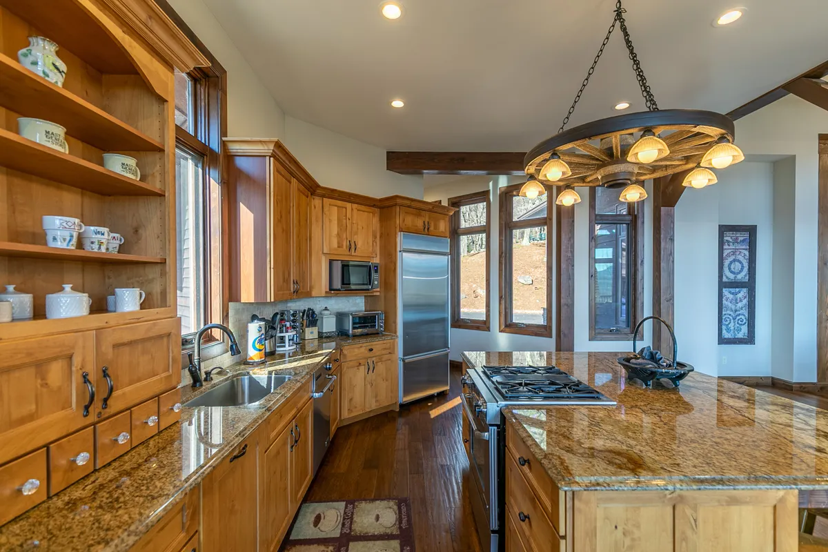 This kitchen features granite countertops, wood cabinetry, a chandelier, and large windows that flood the space with natural light. The layout encourages socializing and family gatherings, embodying a welcoming, homely atmosphere.