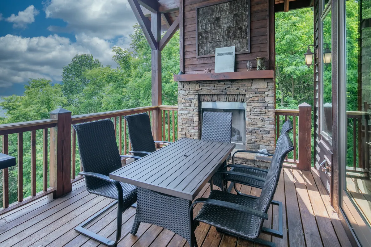 A cozy wooden deck featuring a built-in stone fireplace, surrounded by comfortable outdoor seating and lush greenery. The space is perfect for evening gatherings and enjoying the outdoors year-round.