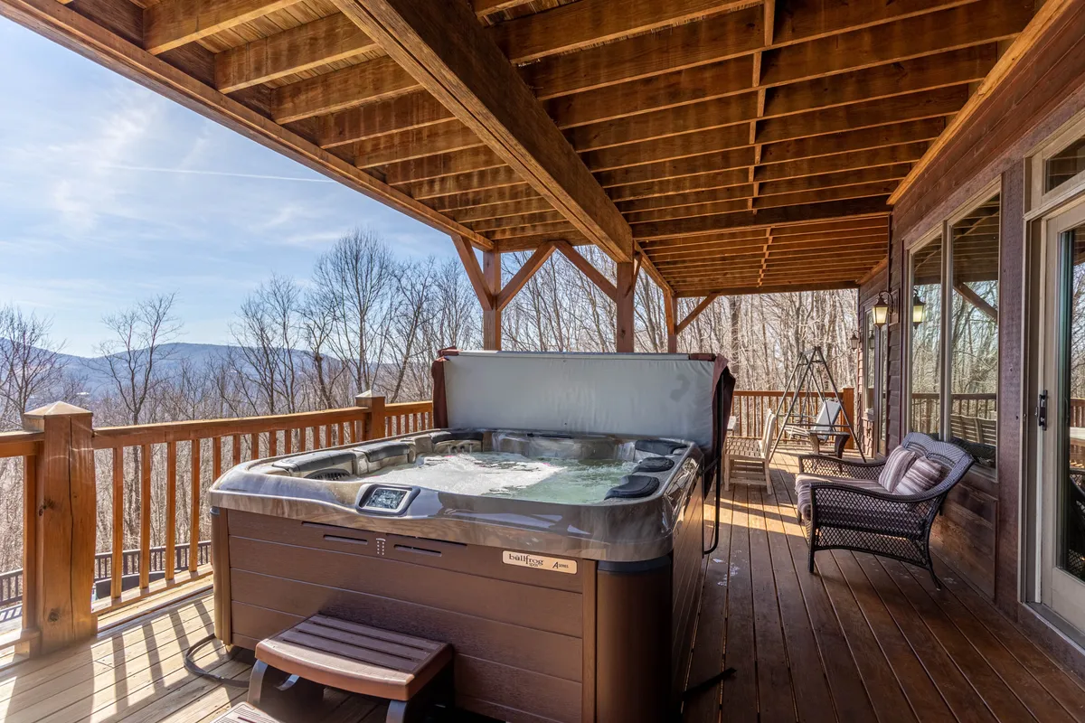 This exterior image features an inviting outdoor hot tub set on a wooden deck, overlooking sweeping mountain views. Friends can be seen relaxing together as the sun sets, with laughter and comfortable conversation filling the air. The tranquil scene is enhanced by the backdrop of the Blue Ridge Mountains.